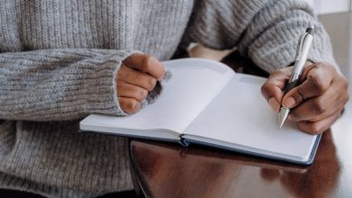 Close-up of unrecognizable black woman writing in journal while sitting at table