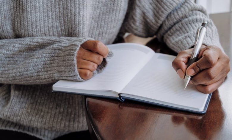 Close-up of unrecognizable black woman writing in journal while sitting at table