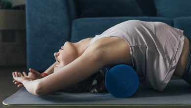 Beautiful fit woman exercising with a blue foam roller at home, pilates concept.