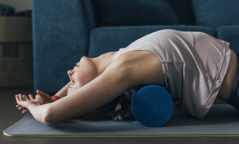 Beautiful fit woman exercising with a blue foam roller at home, pilates concept.