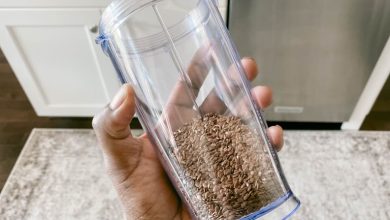 Close-up of woman's hand holding blender cup with whole flaxseed inside; which is healthier, chia or flaxseeds?