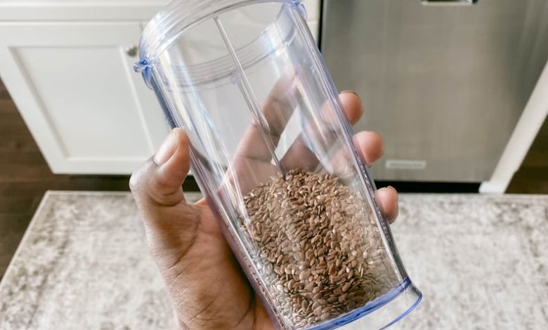 Close-up of woman's hand holding blender cup with whole flaxseed inside; which is healthier, chia or flaxseeds?