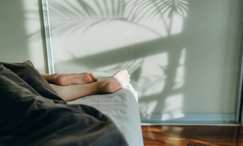 Woman sleeping in bed with feet and legs sticking out from underneath the blanket.