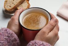 Woman with cup of hot delicious bouillon at white marble table, closeup