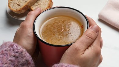 Woman with cup of hot delicious bouillon at white marble table, closeup