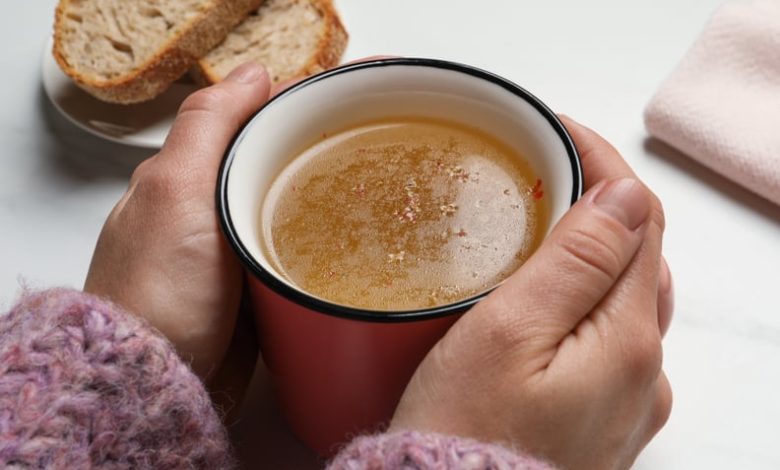 Woman with cup of hot delicious bouillon at white marble table, closeup