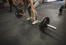 Female cross training ter using a barbell to prefrom a deadlift while at a gym.